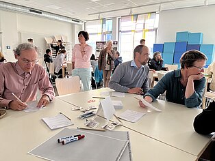 Menschen sitzend an einem Tisch mit Zetteln und Stiften.