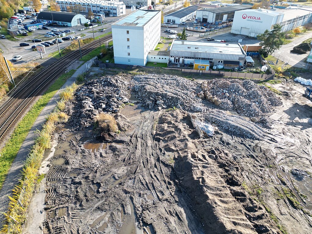 Luftaufnahme der Baustelle am Bauhof mit großen Erdhaufen, Spuren von Baumaschinen und Gebäuden im Hintergrund