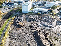 Luftaufnahme der Baustelle am Bauhof mit großen Erdhaufen, Spuren von Baumaschinen und Gebäuden im Hintergrund
