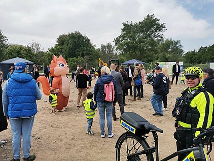 Menschen in bunter Kleidung stehen und gehen auf einem belebten Sandplatz.