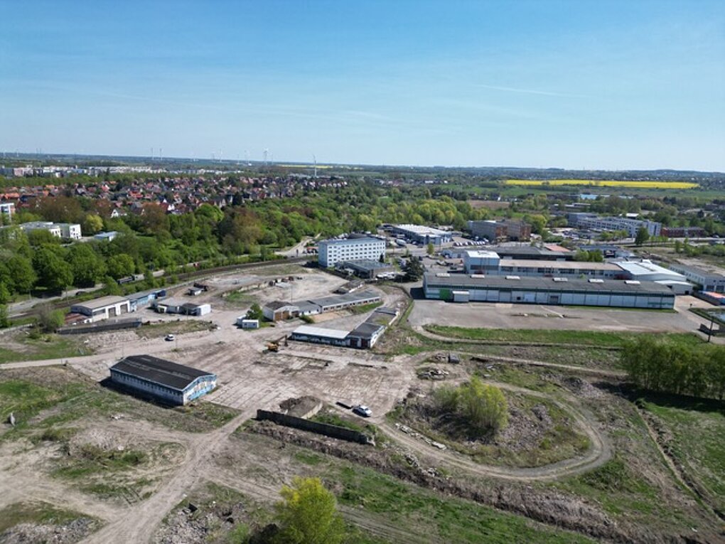 Luftaufnahme des Industrie- und Gewerbegebiets mit mehreren Gebäuden, umgeben von Grünflächen und dem Stadtteil Dierkow im Hintergrund